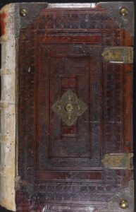 An old, large leather-bound book with ornate metal clasps and corner pieces, featuring intricate embossed designs on the cover and visible wear along the spine.