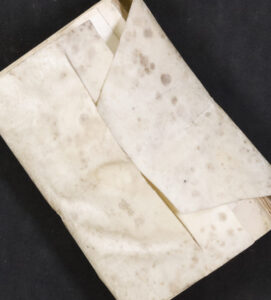 An old book with a mottled, folded parchment wrapper partially covering its cover, set against a black background.